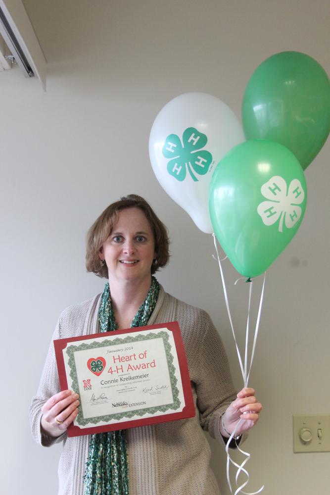 Connie Kreikemeier holding 4-H balloons and a certificate.