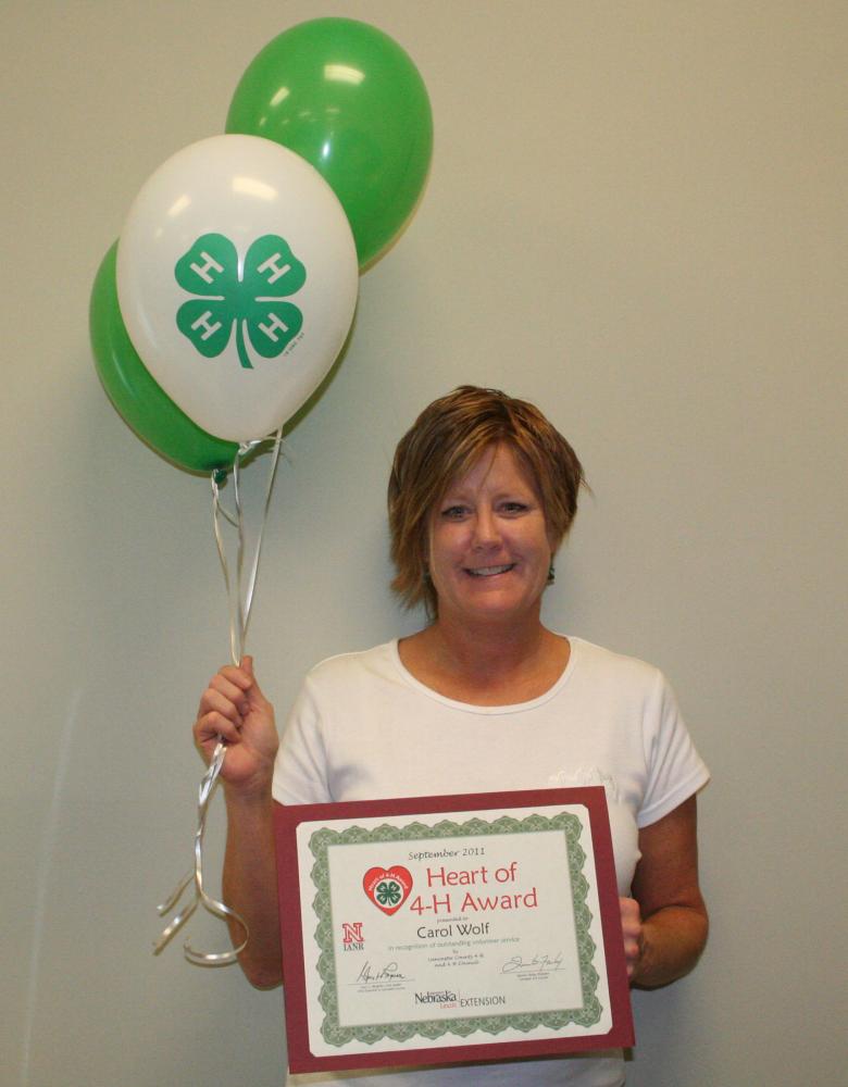 Carol Wolf holding 4-H balloons and a certificate.