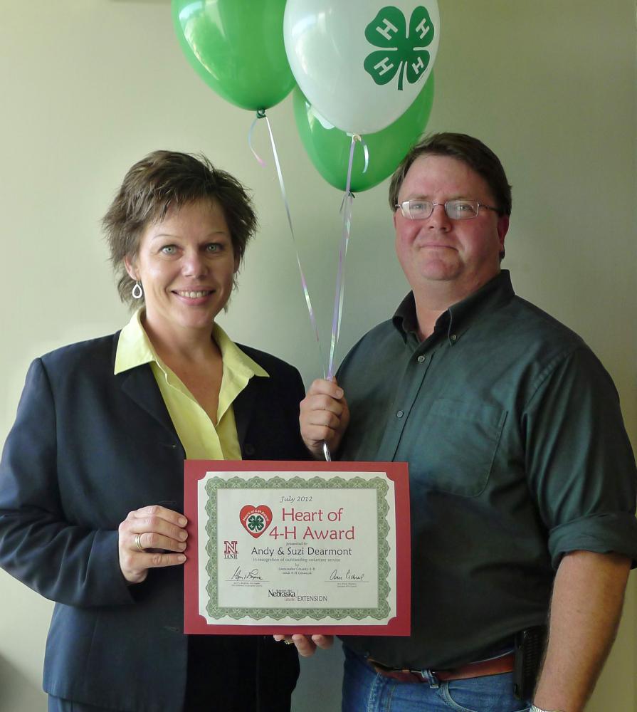 Andy and Suzi Dearmont standing together and holding 4-H balloons and a certificate.