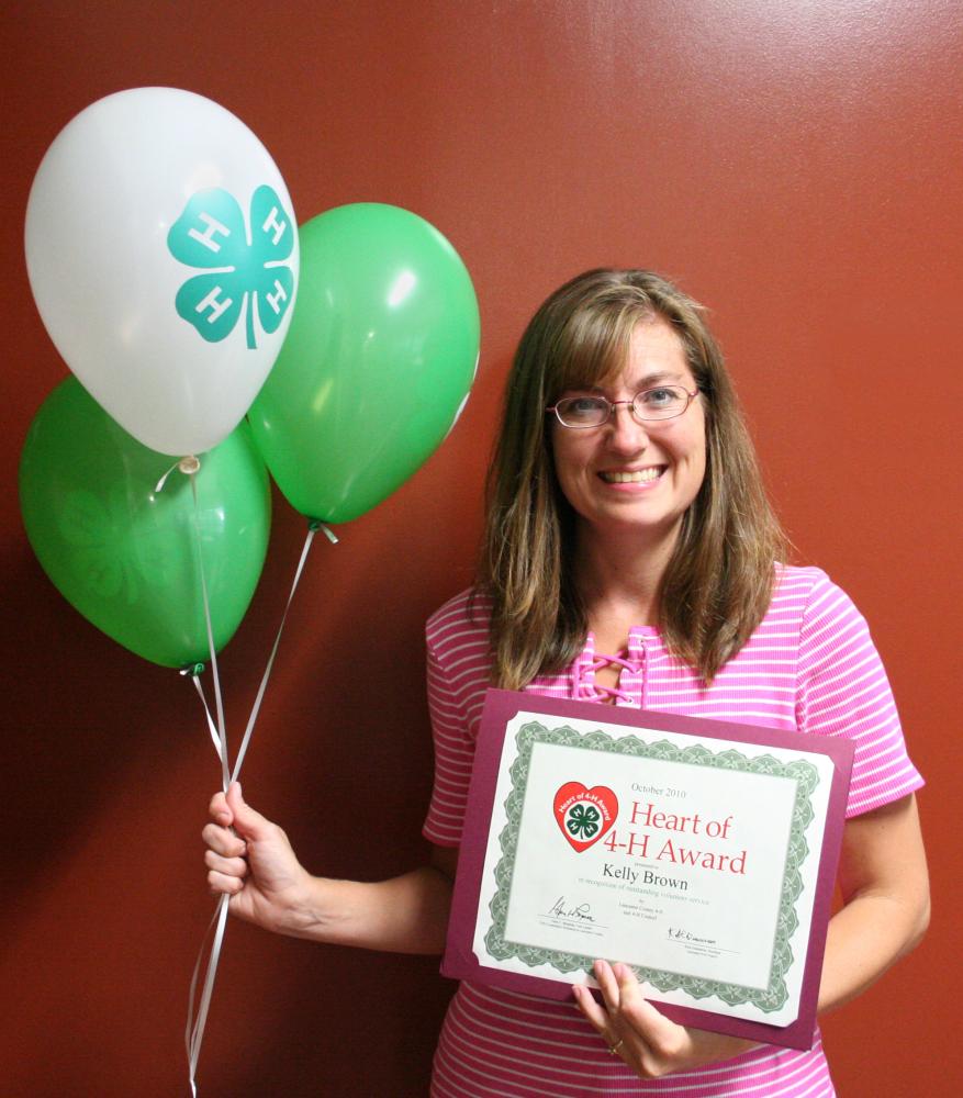 Kelly Brown holding 4-H balloons and a certificate.