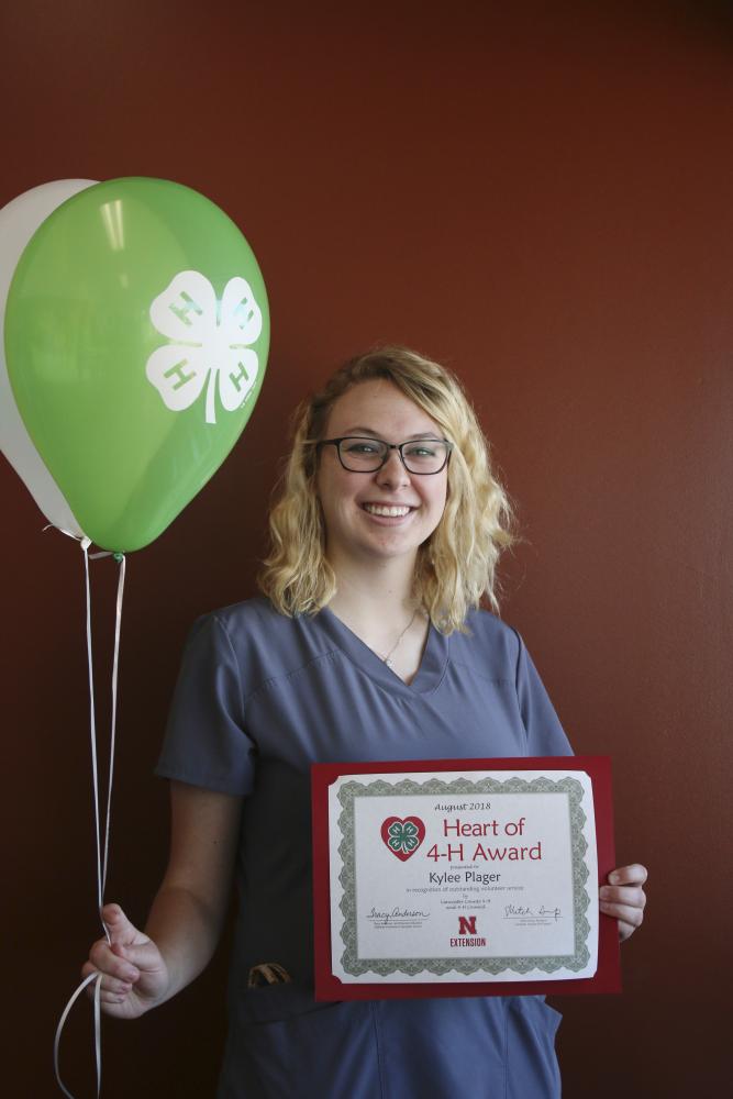 Kylee Plager holding 4-H balloons and a certificate.