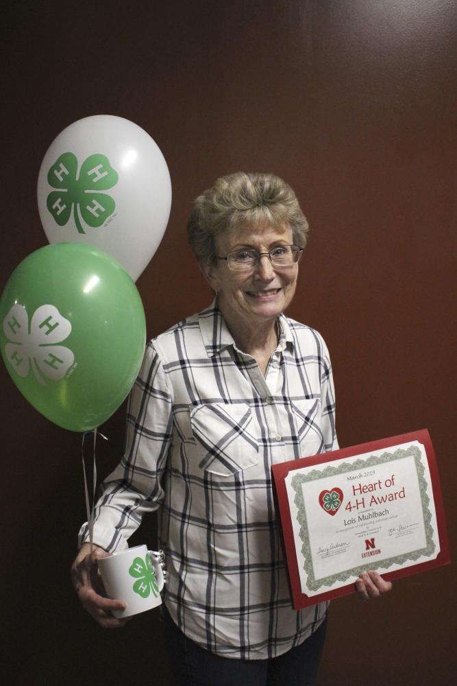 Lois Muhlbach holding 4-H balloons, a 4-H mug, and a certificate.