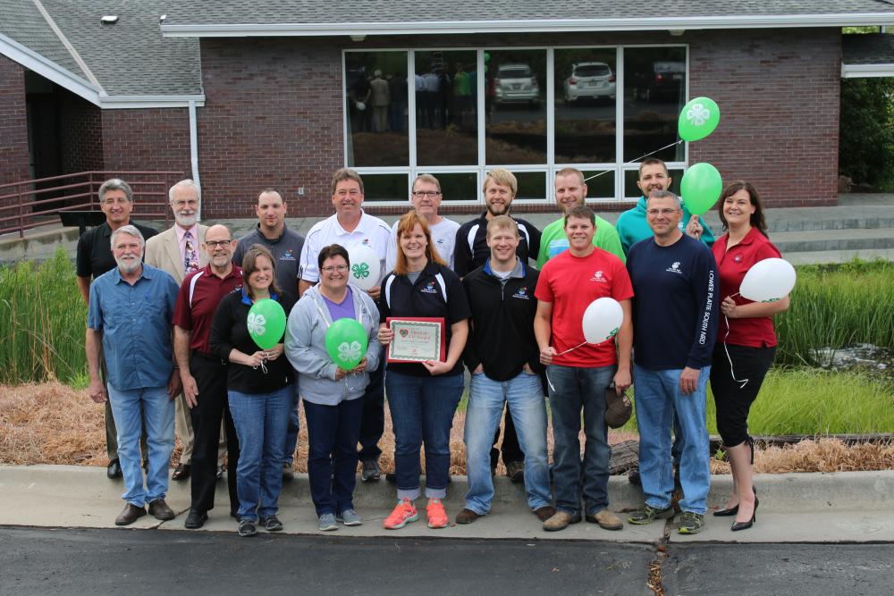 Lower Platte South Natural Resources District (LPSNRD) standing as a group and holding 4-H balloons and a certificate.