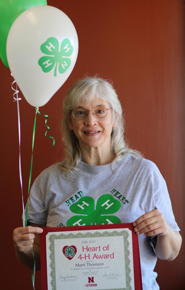 Marti Thomson holding 4-H balloons and a certificate.
