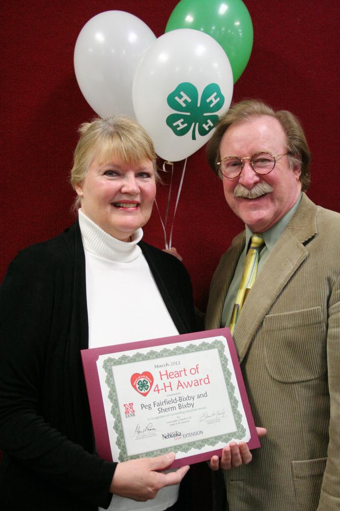 Peg Fairfield-Bixby and Sherm Bixby standing together and holding 4-H balloons and a certificate.