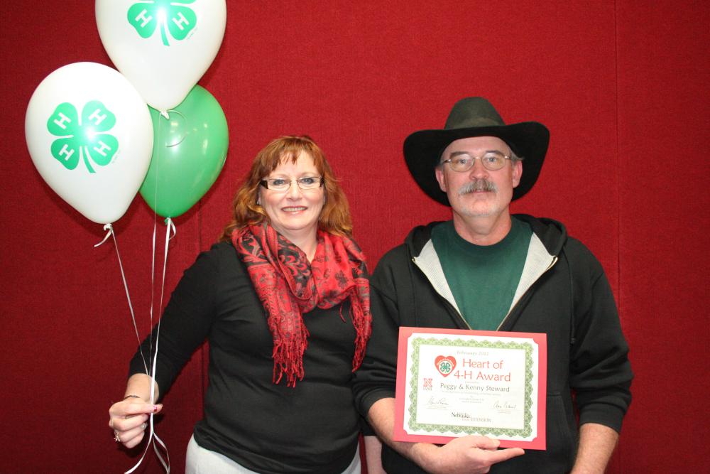 Peggy and Kenny Steward standing together and holding 4-H balloons and a certificate.