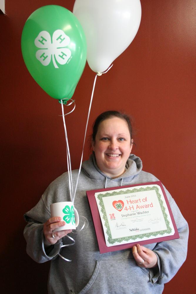 Stephanie Wachter holding a 4-H mug, 4-H balloons, and a certificate.