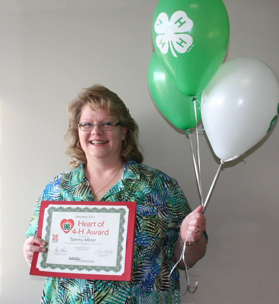 Tammy Miner holding 4-H balloons and a certificate.