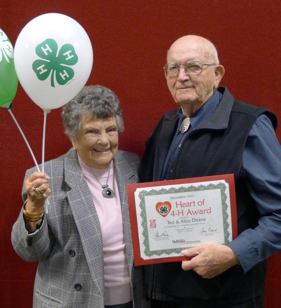 Ted and Alice Doane standing together and holding 4-H balloons and a certificate.