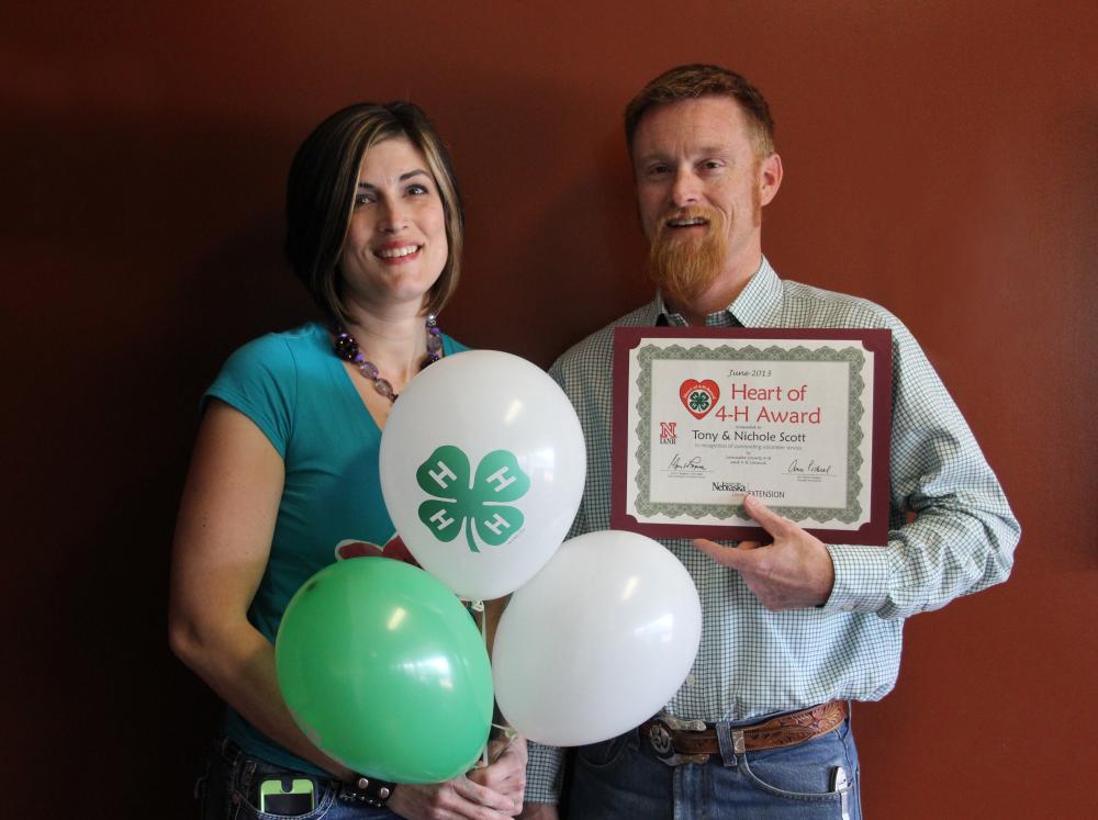 Tony & Nicole Scott standing together and holding 4-H balloons and a certificate.