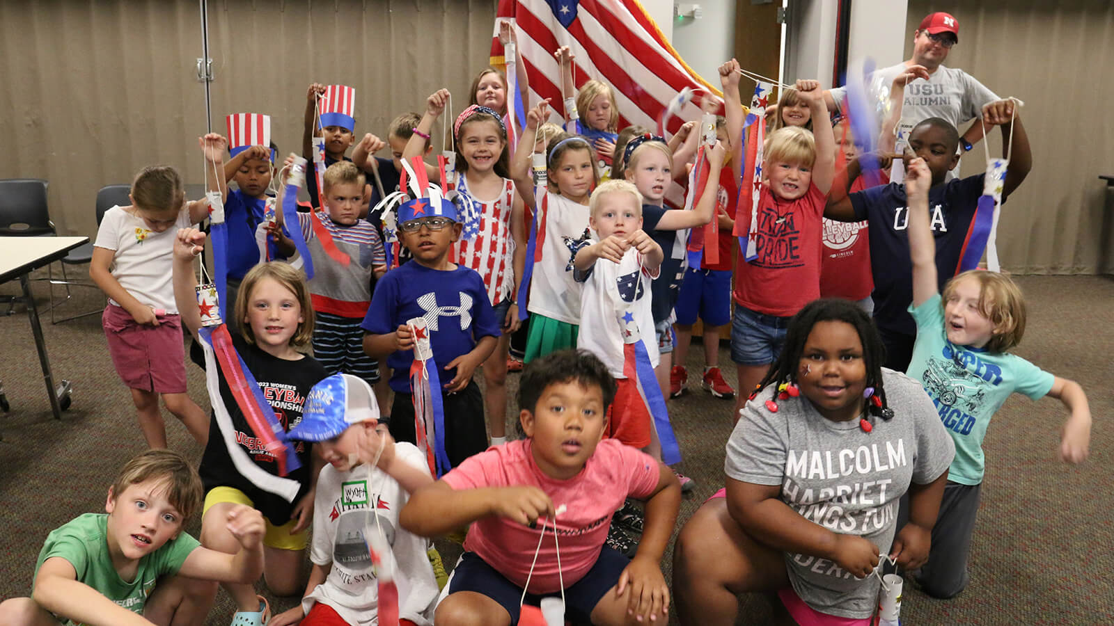 A group of youth and one adult holding handmade patriotic windsocks and some wearing patriotic gear