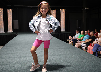 a young girl posing at the end of a runway, wearing a cute outfit