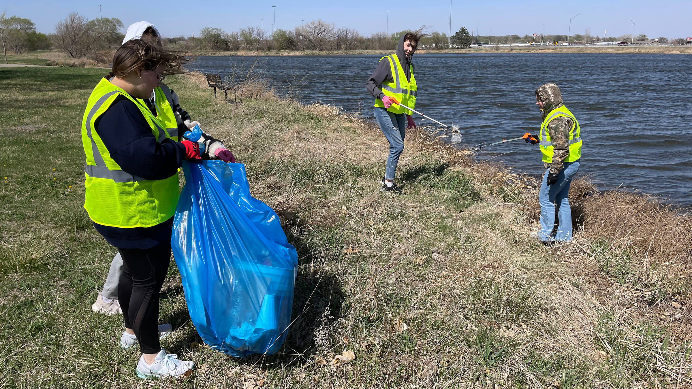 four teen picking up litter with grabber tools and putting into trash bags