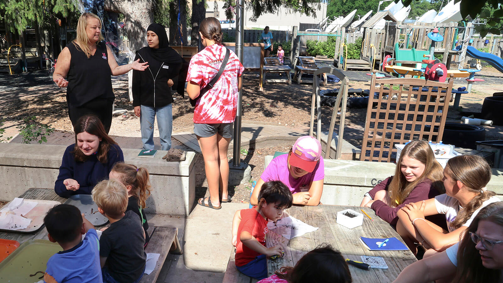 Two adults, several teens and many young children outside looking at worms on picnic tables