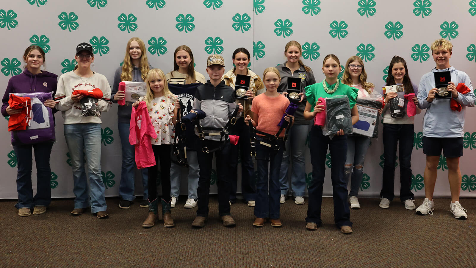 A group of youth holding horse-related items, such as shirts, bits and buckles