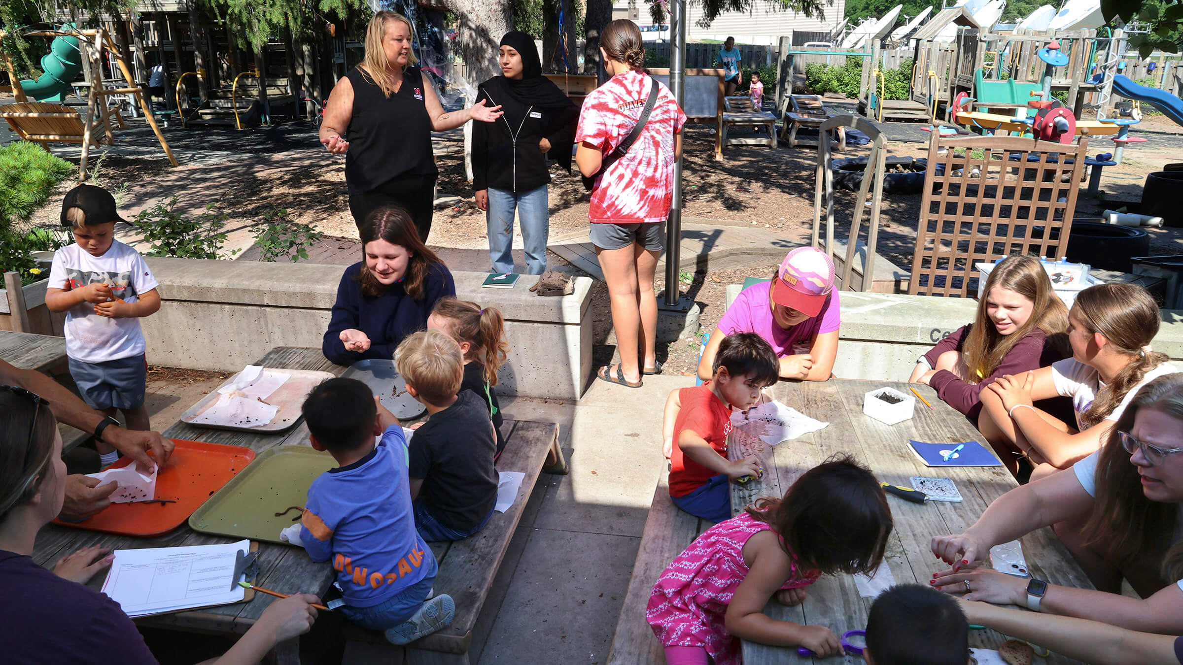 an educator talking to two teenagers with many young children around tables looking at worms