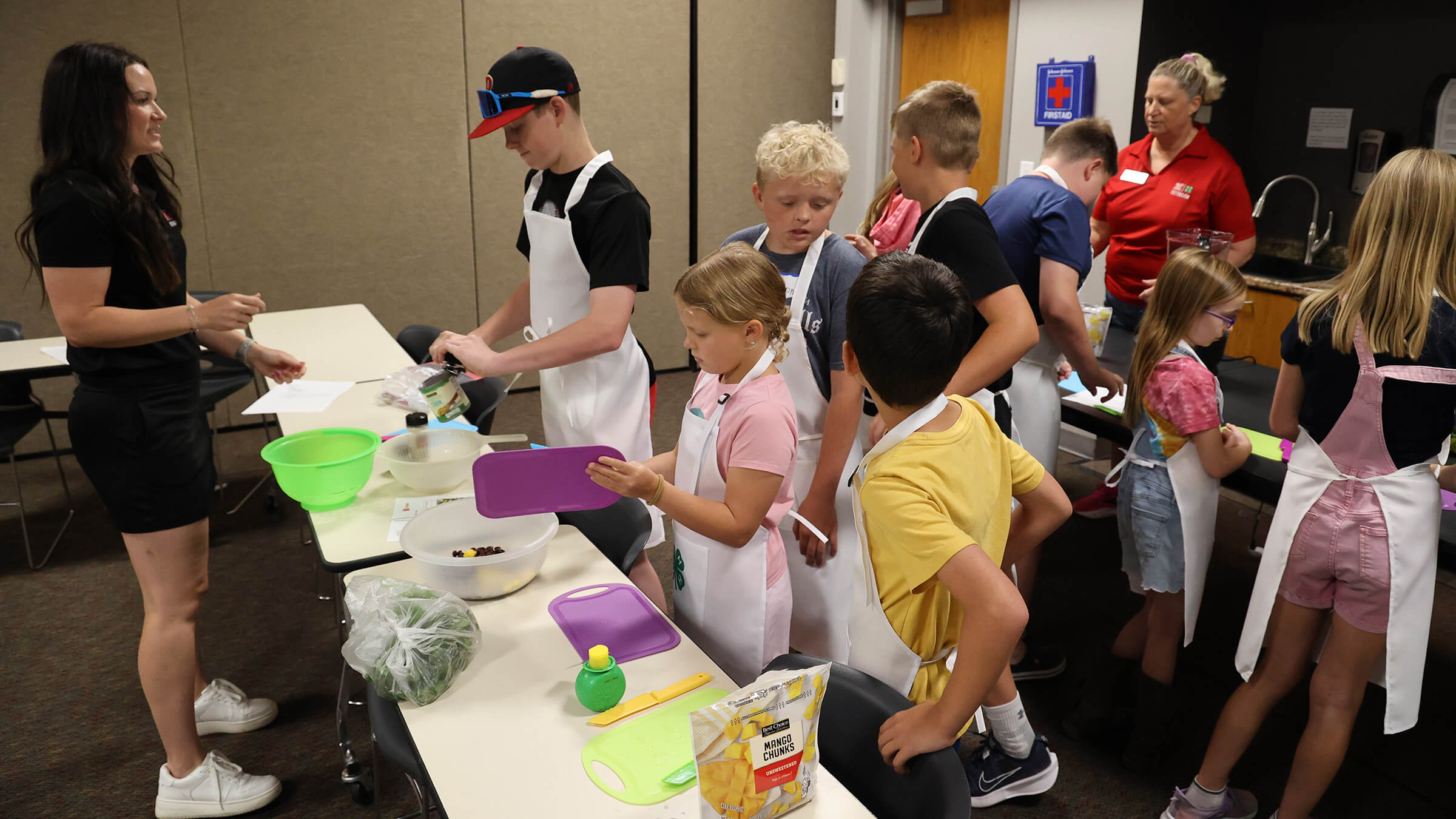 A group of youth in aprons preparing food, with two adults helping