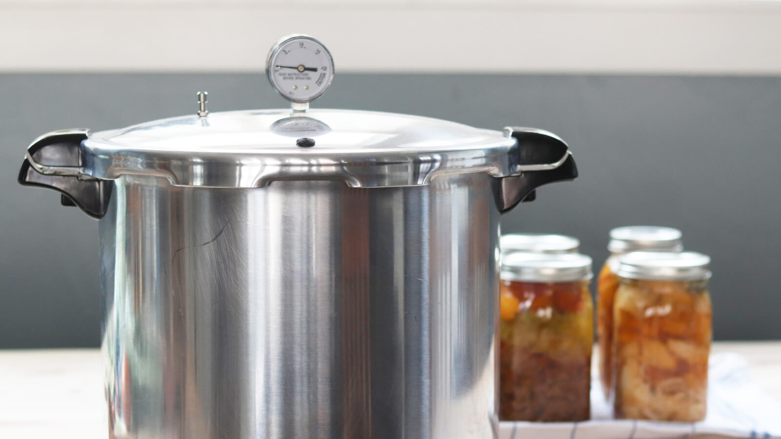 a pressure canner with a dial gauge, next to several jars of canned food 