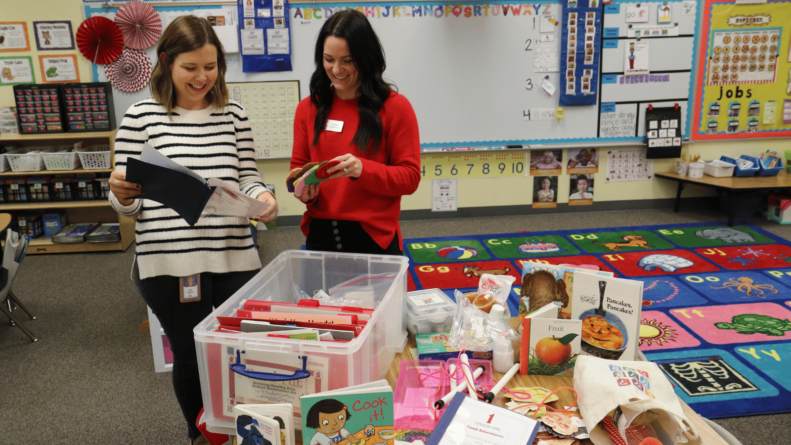 an Extension educator and a teacher looking at a tote full of hands-on activities and books