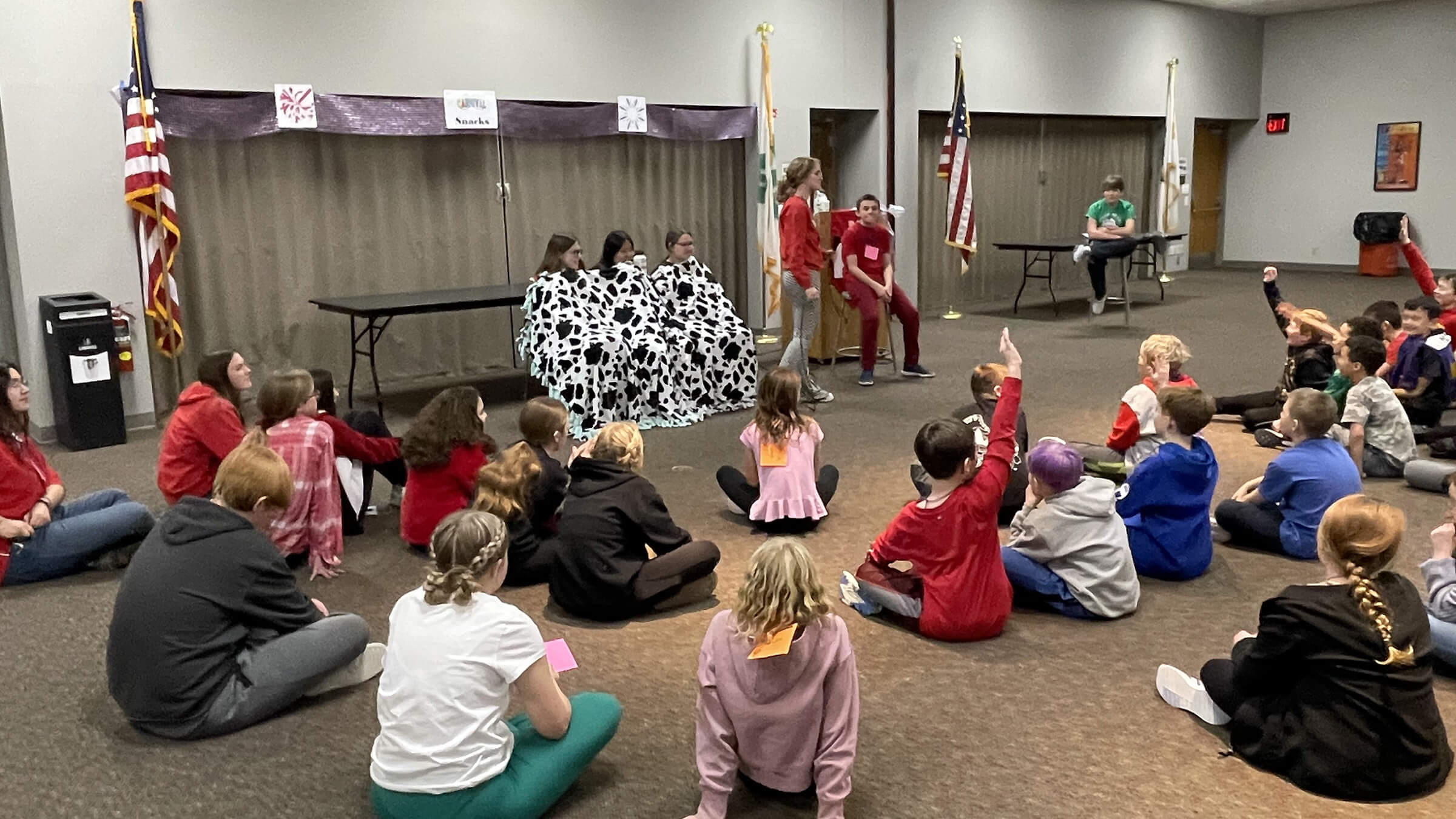 A group of youth sitting on the floor looking a several teens in front of the room leading an activity