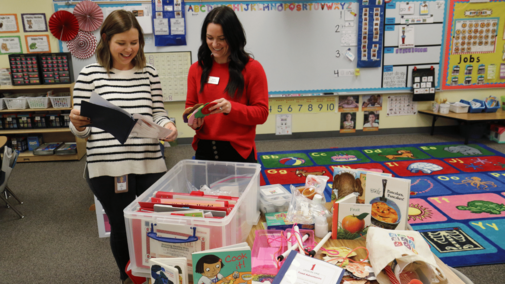 an Extension educator and a teacher looking at a tote full of hands-on activities and books