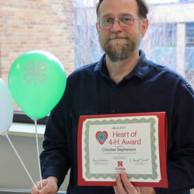 Man holding balloons with 4-H logo and certificate which says Heart of 4-H Award 