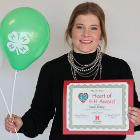 Woman holding balloons with 4-H logo and a certificate that says Heart of 4-H Award