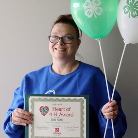 A smiling woman holding two balloons with 4-H logos and a certificate that says Heart of 4-H