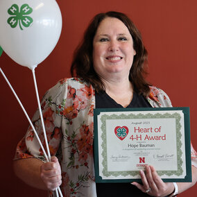 A smiling woman holding two balloons with 4-H logos and a certificate that says Heart of 4-H