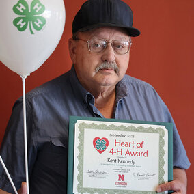 A man holding two balloons with 4-H logos and a certificate that says Heart of 4-H