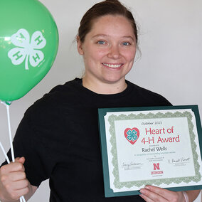 A smiling woman holding two balloons with 4-H logos and a certificate that says Heart of 4-H