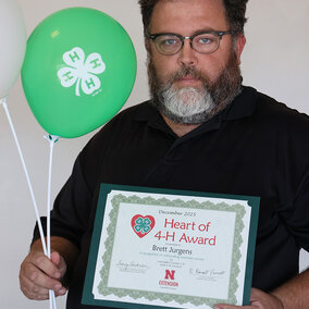 A man holding two balloons with 4-H logos and a certificate that says Heart of 4-H