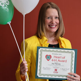 A smiling woman holding two balloons with 4-H logos and a certificate that says Heart of 4-H