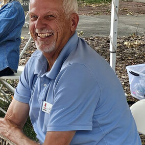 A man smiling outdoors under a booth tent