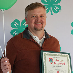 A man holding two balloons with 4-H logos and a certificate that says Heart of 4-H
