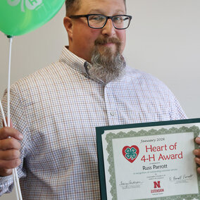 A man holding a balloon with the 4-H logo and a certificate that says Heart of 4-H