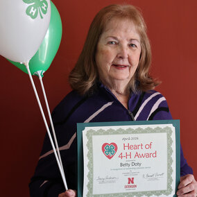 A smiling woman holding two balloons with 4-H logos and a certificate that says Heart of 4-H