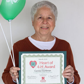 A smiling woman holding two balloons with 4-H logos and a certificate that says Heart of 4-H