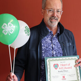 Brad Philson holding 4-H balloons and a Heart of 4-H Award certificate