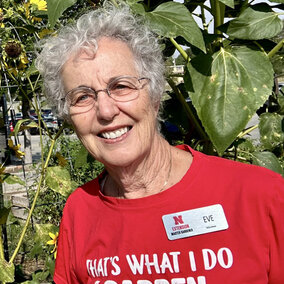 Eve Hoffman wearing a red gardening shirt surrounded by tall sunflowers