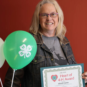 Heart of 4-H Award certificate held beside green and white balloons, red background.