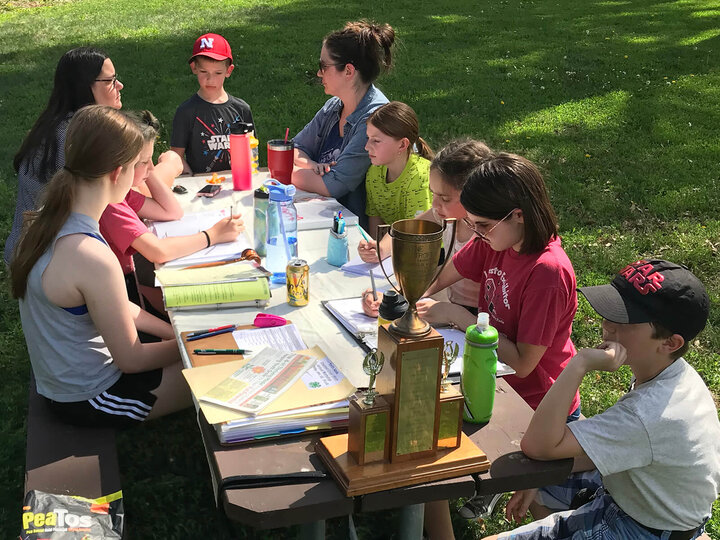 adults and youth sitting at a picnic table with a lot of books and papers in front of them