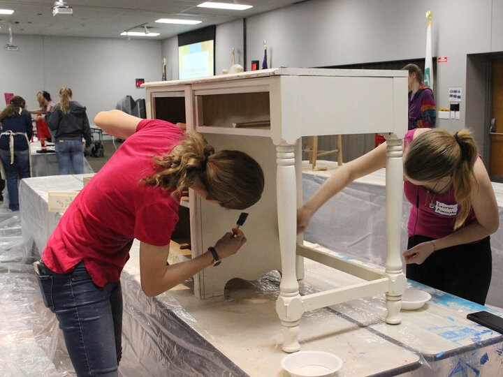 several youth painting furniture on tables draped with plastic