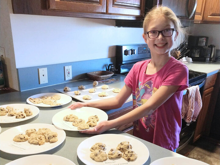 A teenage girl in a kitchen with several plates of cookies