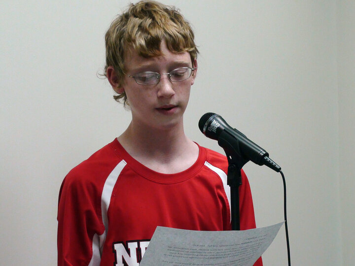 teen boy speaking into a microphone, looking at a sheet of paper