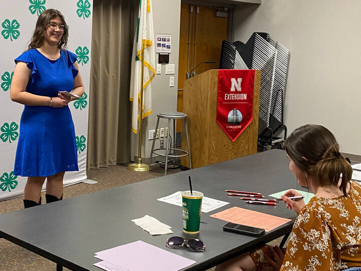 A teen girl holding note cards, smiling and facing an adult judge sitting at a table