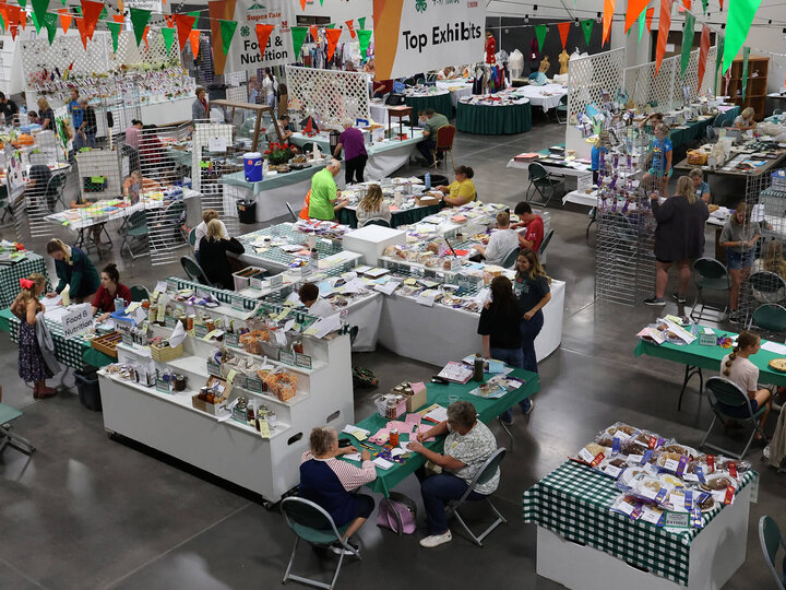 Large room with people among displays full of fair exhibits, including various food items