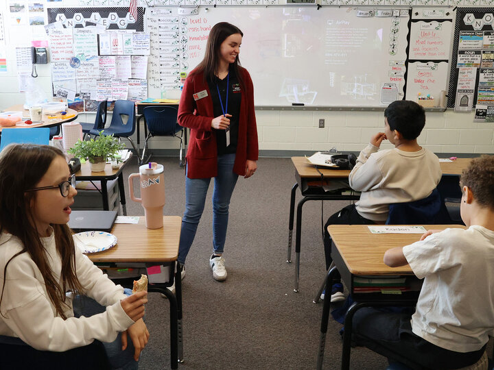 A woman smiling at students eating veggie roll ups in a classroom