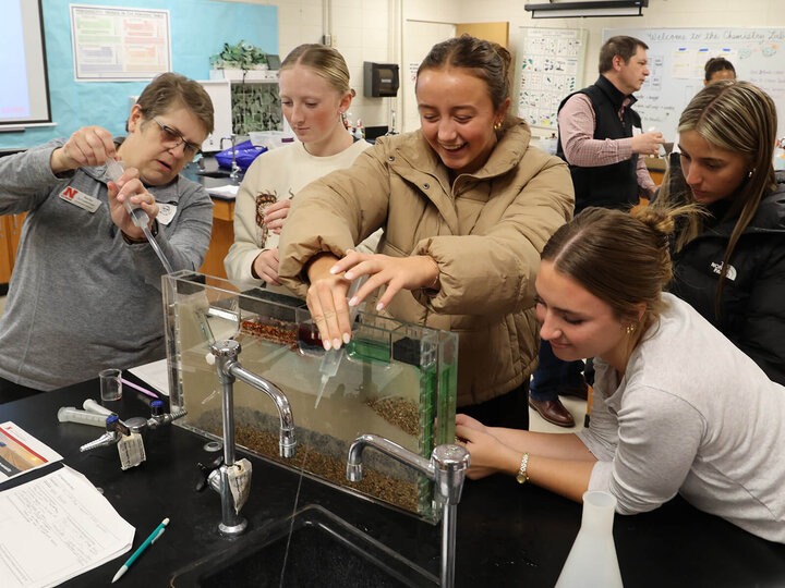 An adult woman and four teenage girls pumping water into a waterflow model in a science classroom