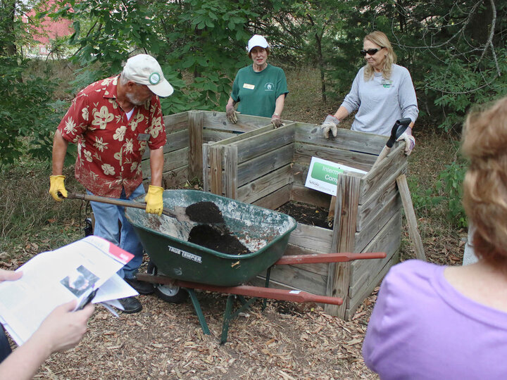 Three people standing around two square wood bins, one male shoveling compost into a wheelbarrel